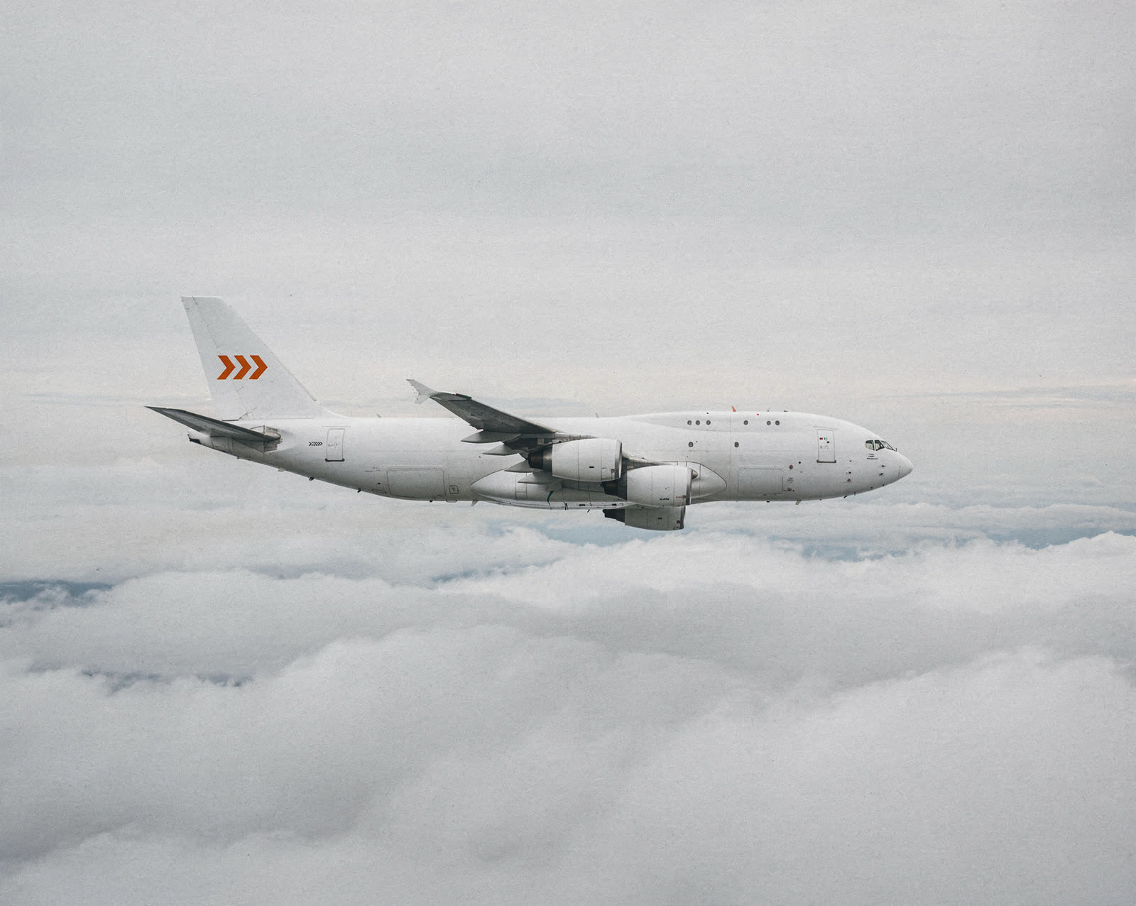A white cargo freighter with orange chevrons on its tail flying above the clouds